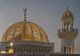 Illuminated golden dome and minaret of mosque at dusk in oman 