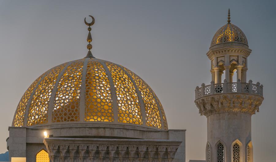 Illuminated golden dome and minaret of mosque at dusk in oman 